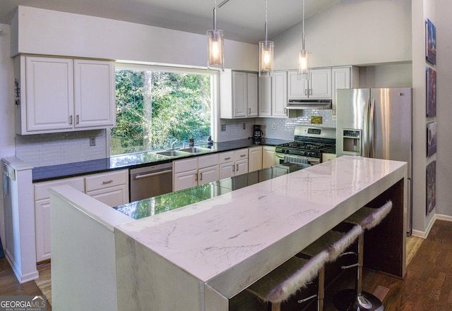 kitchen with appliances with stainless steel finishes, sink, dark stone countertops, white cabinetry, and lofted ceiling