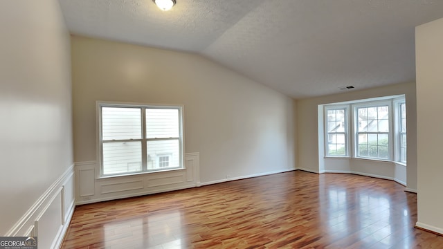 empty room featuring a textured ceiling, light wood-type flooring, and lofted ceiling