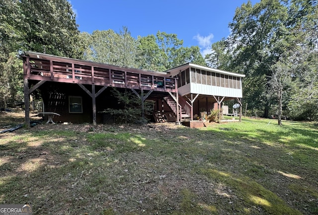 rear view of house featuring a lawn, a wooden deck, and a sunroom