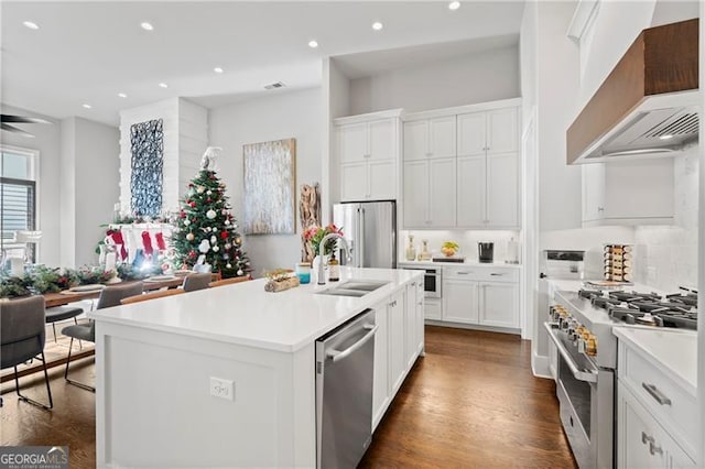 kitchen with white cabinets, an island with sink, wall chimney range hood, and appliances with stainless steel finishes