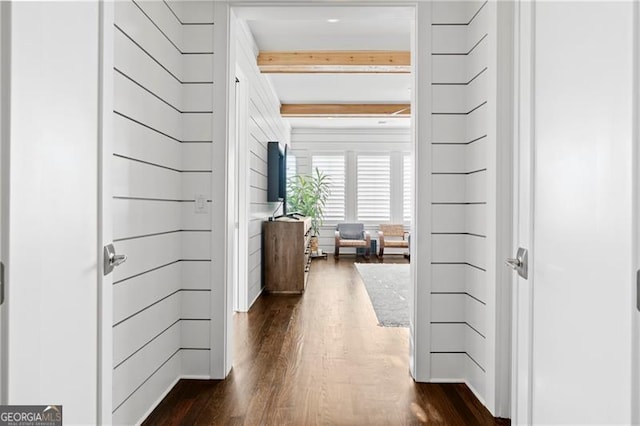 corridor with beamed ceiling, wood walls, and dark wood-type flooring