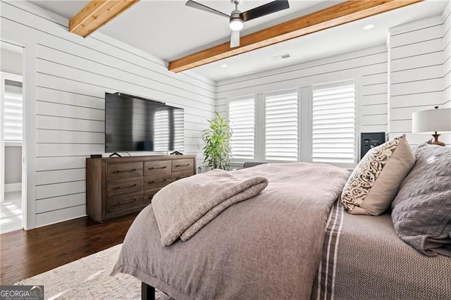 bedroom featuring ceiling fan, beamed ceiling, dark wood-type flooring, and wood walls