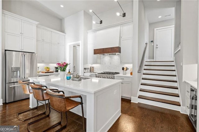 kitchen with custom exhaust hood, a kitchen island with sink, white cabinets, sink, and appliances with stainless steel finishes