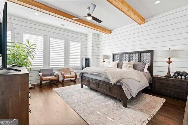 bedroom with beam ceiling, ceiling fan, dark wood-type flooring, and wood walls