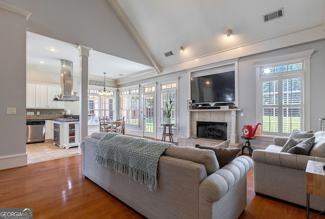 living room featuring lofted ceiling with beams, light hardwood / wood-style flooring, a notable chandelier, and a tiled fireplace