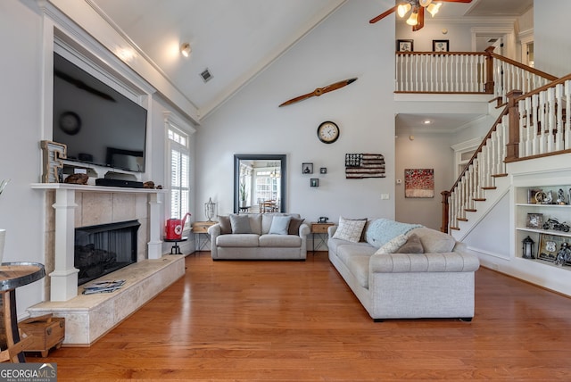 living room with ornamental molding, ceiling fan, a tile fireplace, high vaulted ceiling, and light hardwood / wood-style floors