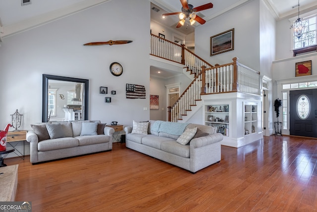 living room featuring a towering ceiling, wood-type flooring, and ornamental molding