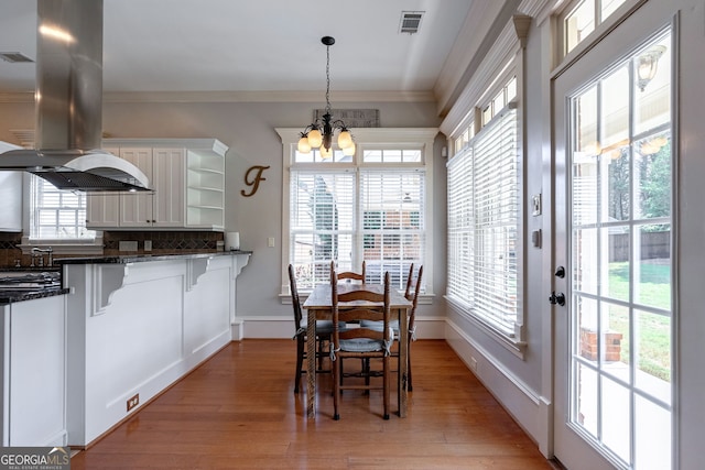 dining area with light wood-type flooring, crown molding, and a chandelier