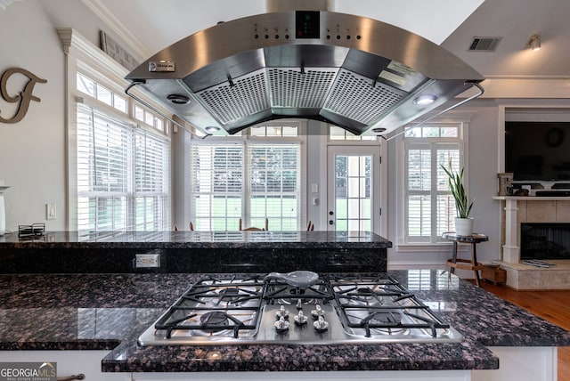 kitchen with island exhaust hood, a wealth of natural light, stainless steel gas stovetop, and a tiled fireplace