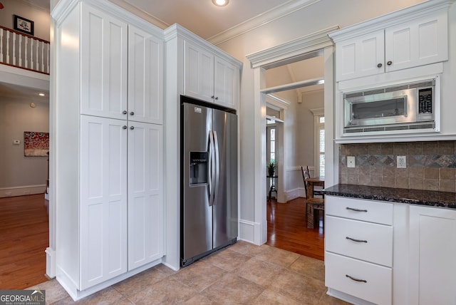 kitchen featuring white cabinets, appliances with stainless steel finishes, ornamental molding, and dark stone countertops