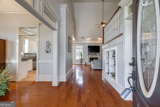 entryway with ceiling fan, wood-type flooring, ornamental molding, and a tile fireplace