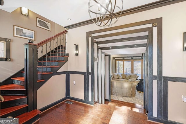 entrance foyer with a chandelier, wood-type flooring, and crown molding