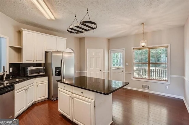 kitchen featuring appliances with stainless steel finishes, a textured ceiling, sink, a center island, and white cabinetry