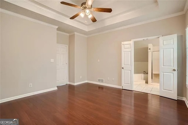 unfurnished bedroom featuring a tray ceiling, connected bathroom, ceiling fan, and ornamental molding