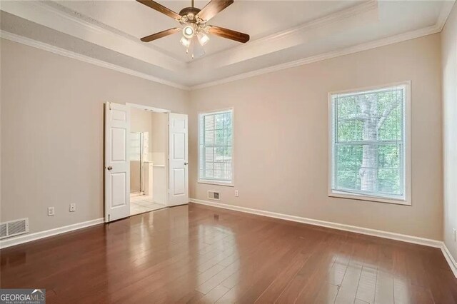 spare room featuring dark wood-type flooring, a raised ceiling, ceiling fan, and ornamental molding