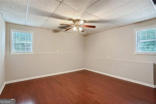 unfurnished room with a wealth of natural light, dark hardwood / wood-style flooring, a drop ceiling, and ceiling fan