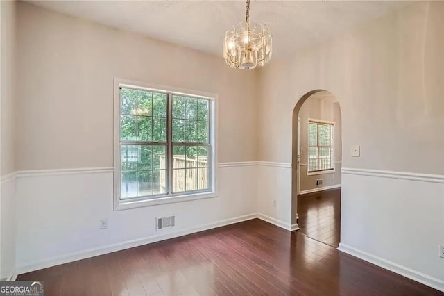 spare room featuring a chandelier and dark wood-type flooring