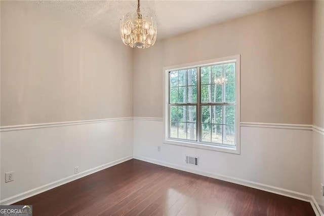 spare room with dark hardwood / wood-style floors and an inviting chandelier