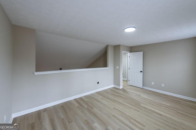 additional living space featuring light hardwood / wood-style floors, lofted ceiling, and a textured ceiling