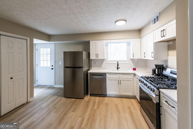 kitchen with sink, a healthy amount of sunlight, stainless steel appliances, a textured ceiling, and white cabinets