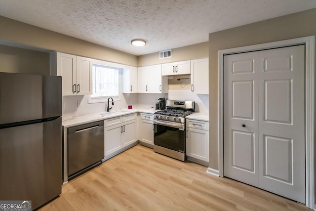 kitchen with white cabinets, sink, a textured ceiling, light hardwood / wood-style floors, and stainless steel appliances