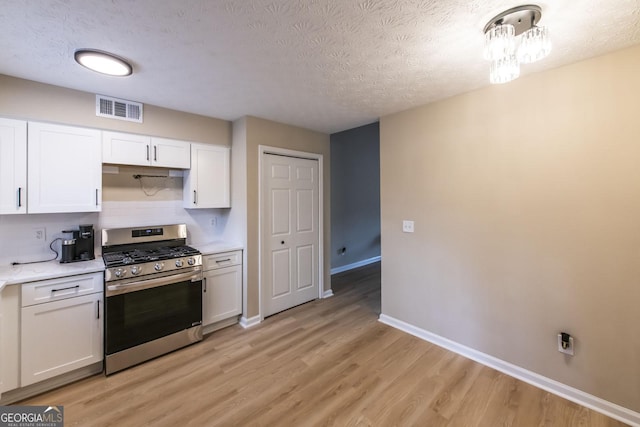 kitchen featuring a textured ceiling, stainless steel gas stove, light hardwood / wood-style floors, and white cabinetry