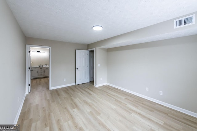 unfurnished bedroom featuring a textured ceiling, light hardwood / wood-style floors, and connected bathroom