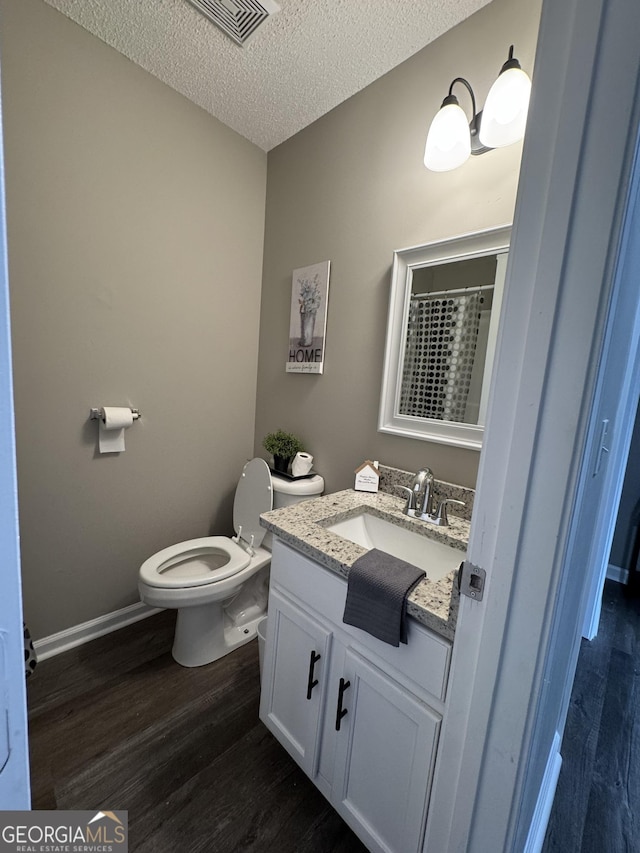 bathroom featuring a shower with shower curtain, vanity, a textured ceiling, hardwood / wood-style flooring, and toilet