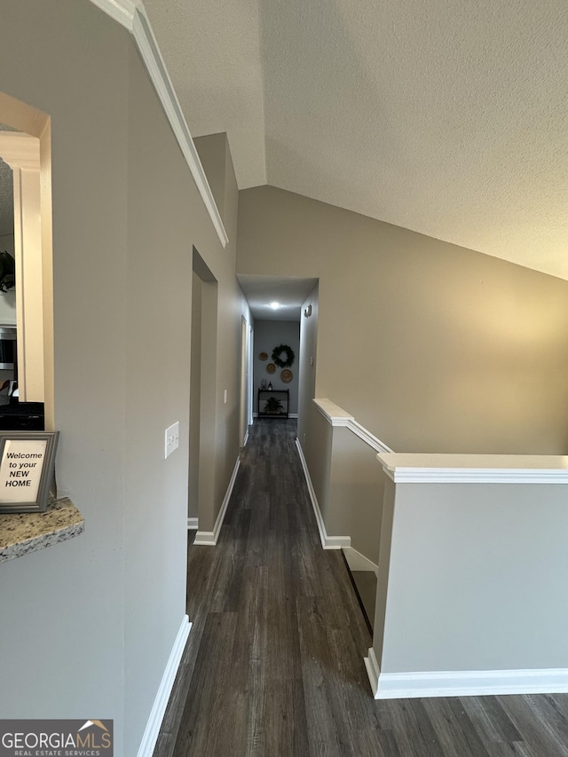 corridor with a textured ceiling, dark wood-type flooring, and vaulted ceiling