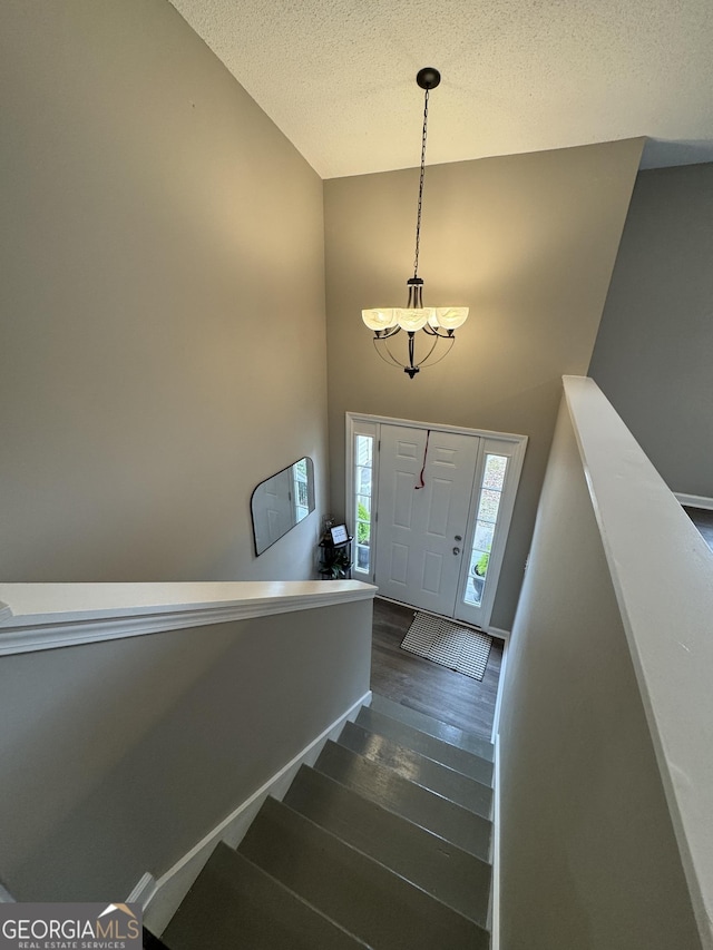 foyer entrance with a textured ceiling, a towering ceiling, dark wood-type flooring, and an inviting chandelier