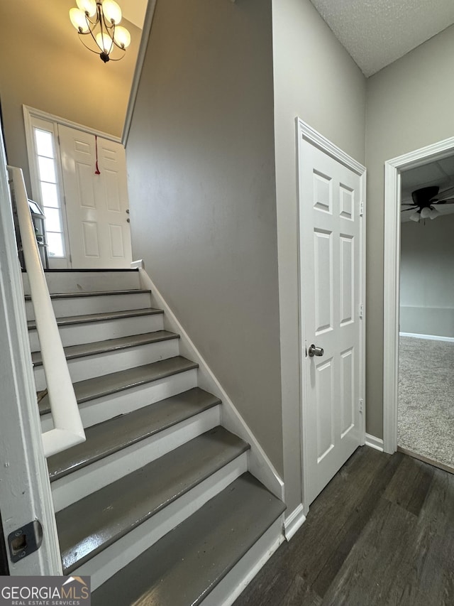 stairs with ceiling fan with notable chandelier, wood-type flooring, and a textured ceiling