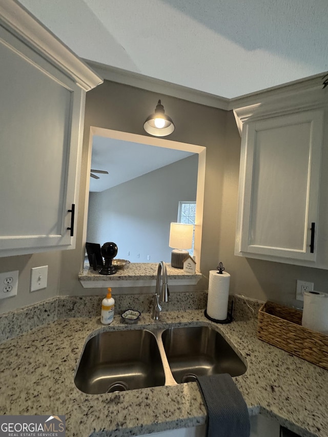 kitchen with white cabinets, light stone counters, and sink