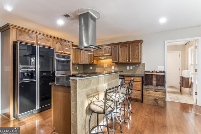 kitchen featuring a kitchen island, island exhaust hood, tasteful backsplash, light hardwood / wood-style floors, and black fridge with ice dispenser