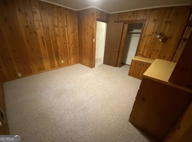 unfurnished bedroom with a closet, ornamental molding, light colored carpet, and wooden walls