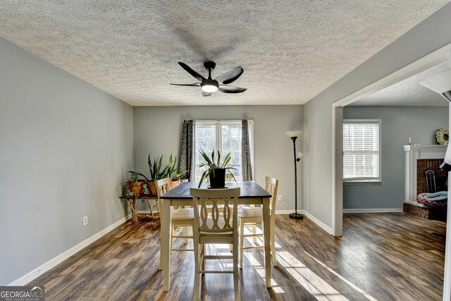 dining room with ceiling fan, dark hardwood / wood-style flooring, a textured ceiling, and a brick fireplace