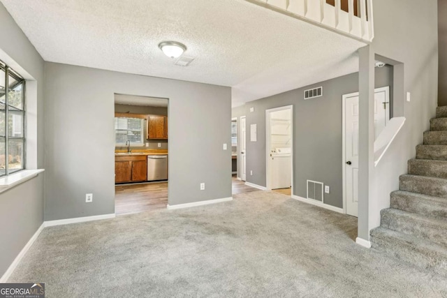 unfurnished living room with a textured ceiling, light colored carpet, and sink