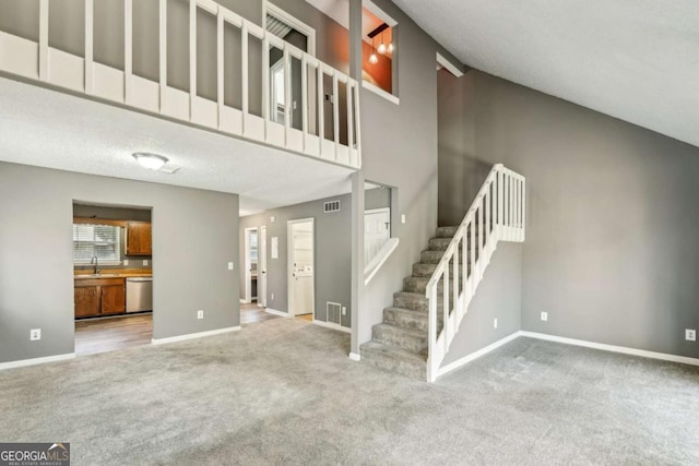 unfurnished living room featuring a towering ceiling, sink, and carpet