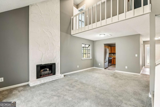 unfurnished living room featuring carpet, a stone fireplace, and a high ceiling