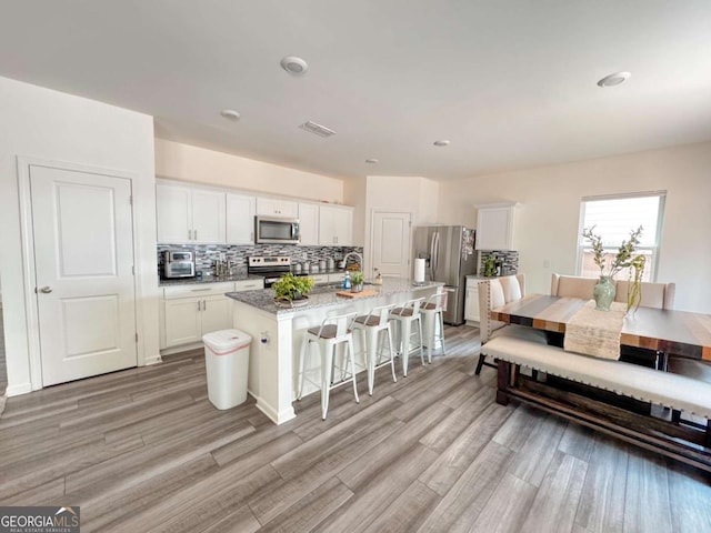 kitchen with white cabinetry, a kitchen island with sink, a breakfast bar area, and appliances with stainless steel finishes