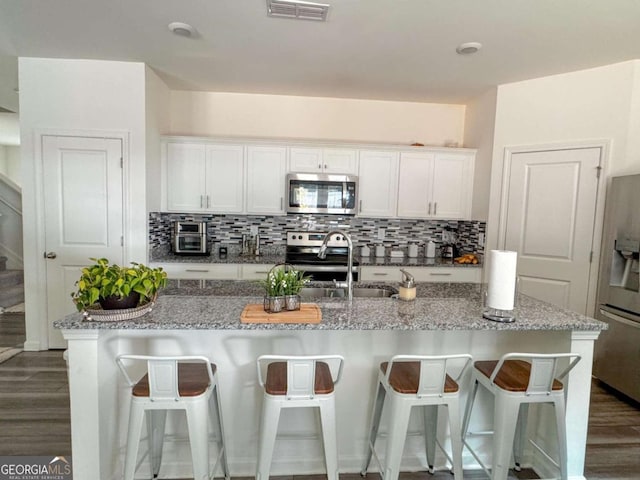 kitchen with light stone countertops, white cabinetry, an island with sink, and stainless steel appliances