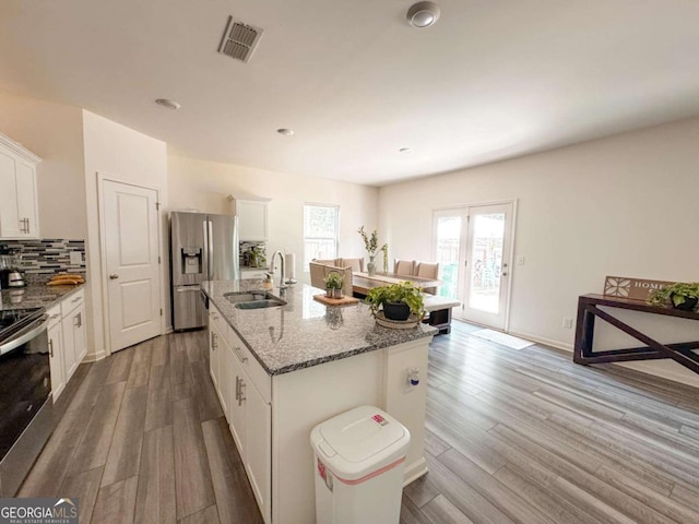 kitchen featuring white cabinetry, sink, stainless steel appliances, light stone counters, and a kitchen island with sink