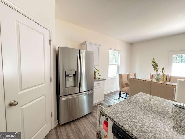 kitchen with light stone countertops, stainless steel refrigerator with ice dispenser, light wood-type flooring, and white cabinetry