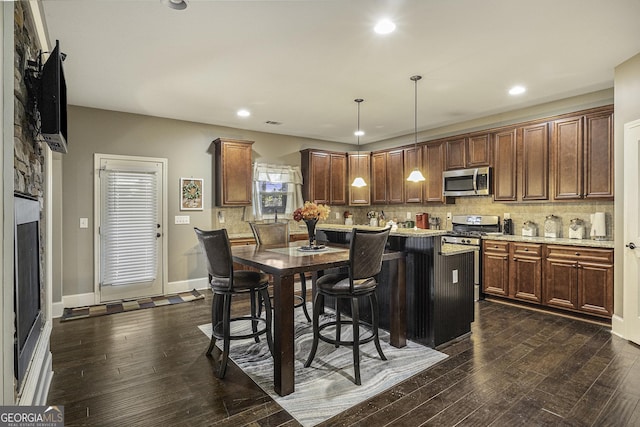 kitchen featuring a center island, dark wood-type flooring, appliances with stainless steel finishes, decorative light fixtures, and a breakfast bar area