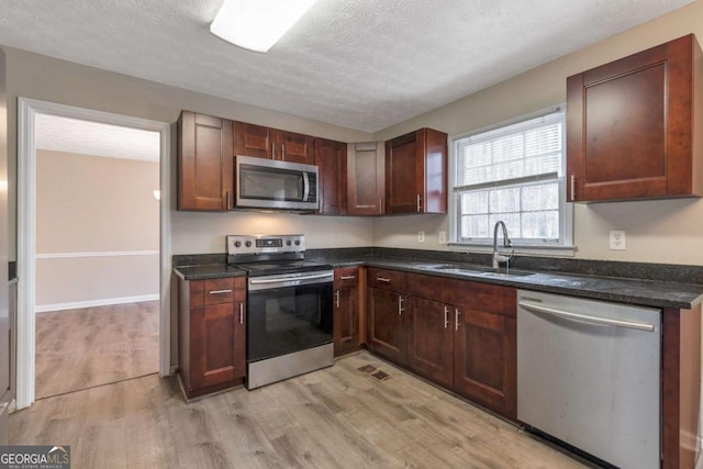 kitchen featuring dark stone counters, sink, light wood-type flooring, a textured ceiling, and stainless steel appliances