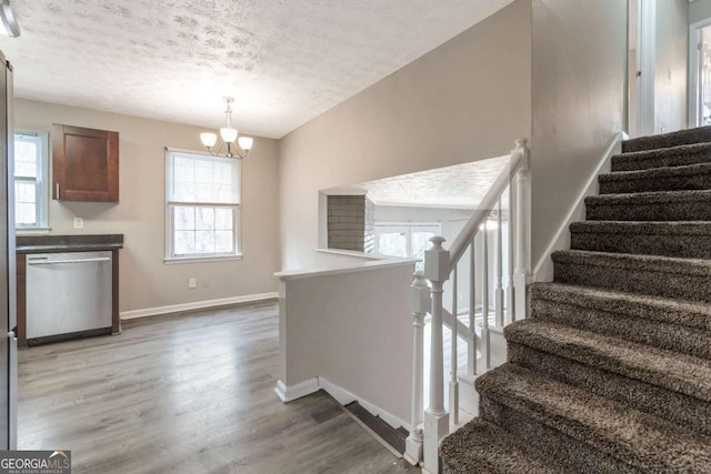 staircase featuring a chandelier, wood-type flooring, a textured ceiling, and a healthy amount of sunlight