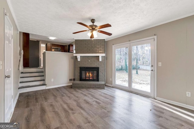 unfurnished living room featuring light hardwood / wood-style flooring, ceiling fan, ornamental molding, a fireplace, and a textured ceiling