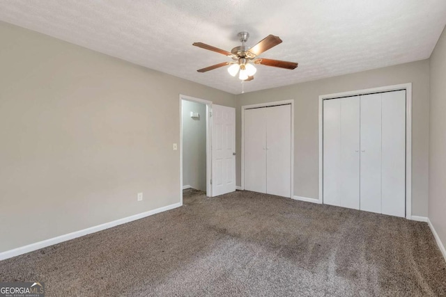 unfurnished bedroom featuring two closets, a textured ceiling, carpet floors, and ceiling fan