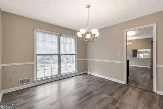 unfurnished dining area with a textured ceiling, plenty of natural light, dark wood-type flooring, and ceiling fan with notable chandelier