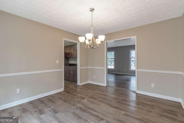 unfurnished dining area with a textured ceiling, hardwood / wood-style flooring, and a notable chandelier