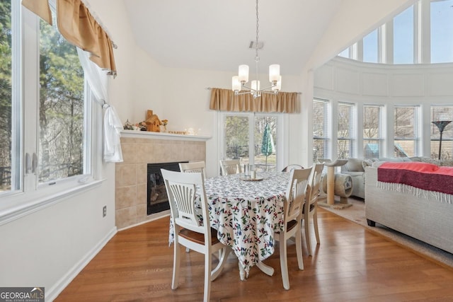 dining space with a wealth of natural light, a fireplace, wood-type flooring, and a notable chandelier